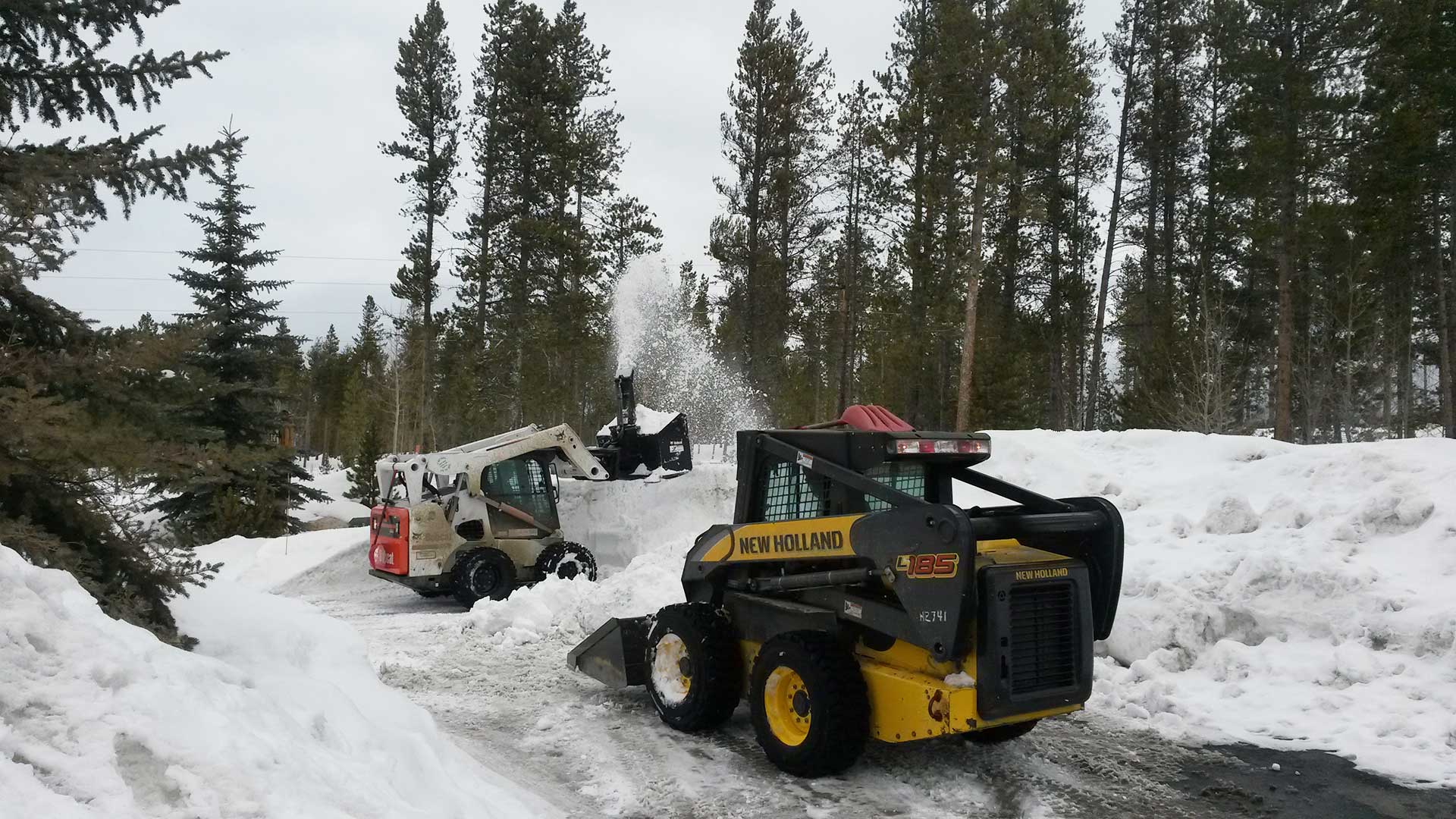 Company skid loaders clearing snow from a customer's property.